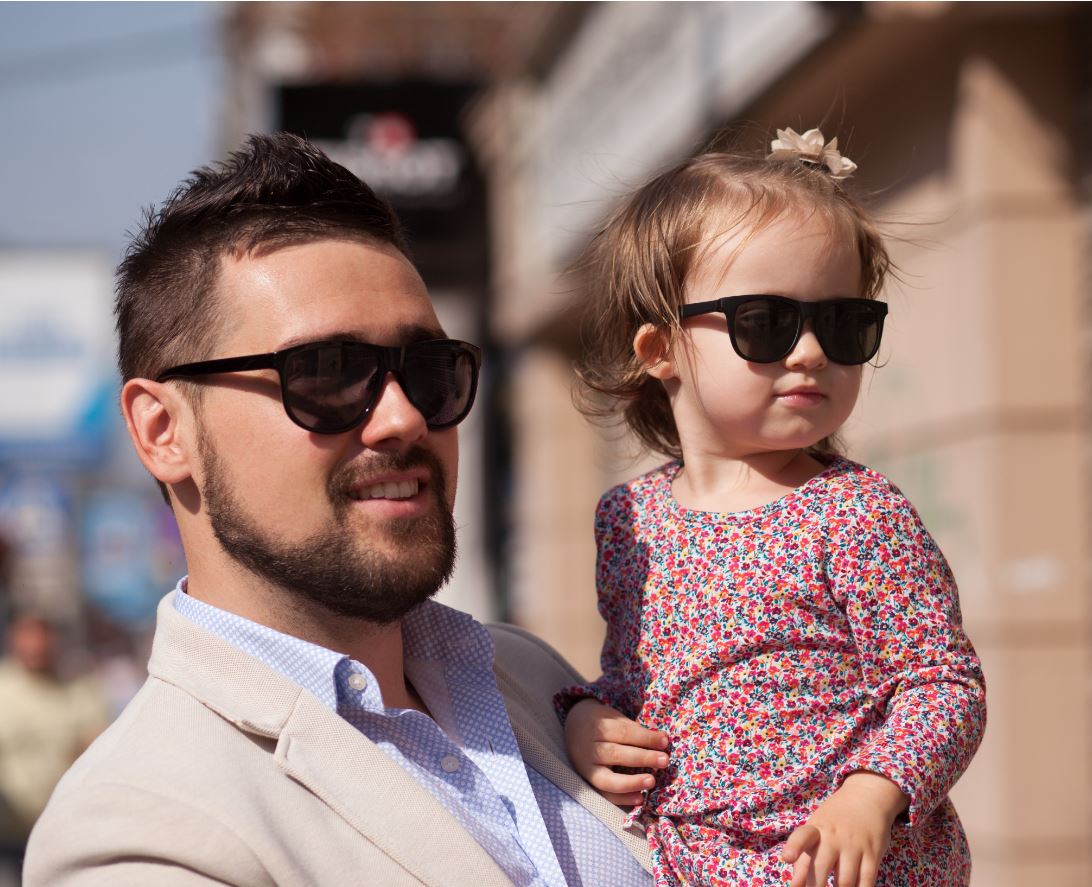 papà con bambina in braccio entrambi indossano occhiali da sole